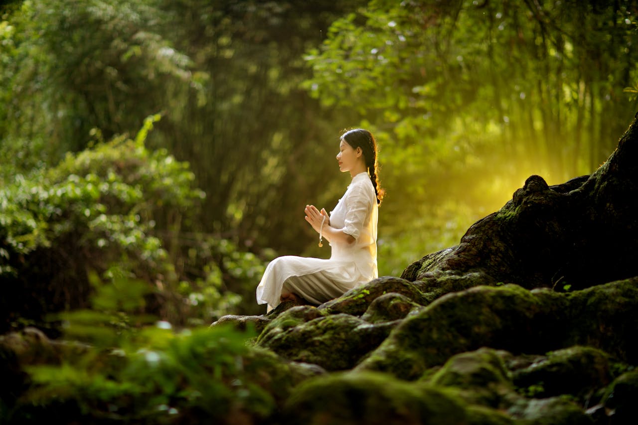 A woman meditating outdoors with prayer beads amidst lush forest greenery.