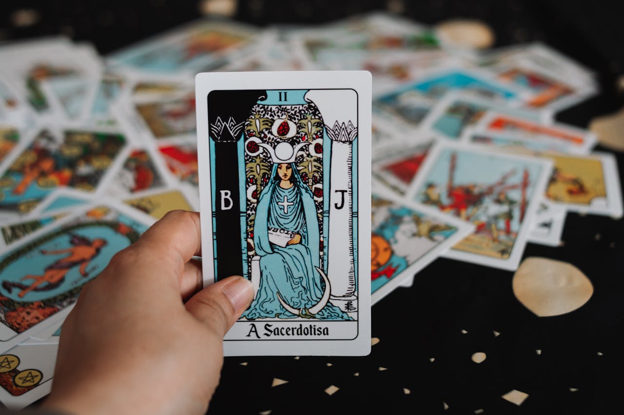 Close-up of a hand holding The High Priestess tarot card among scattered tarot cards.