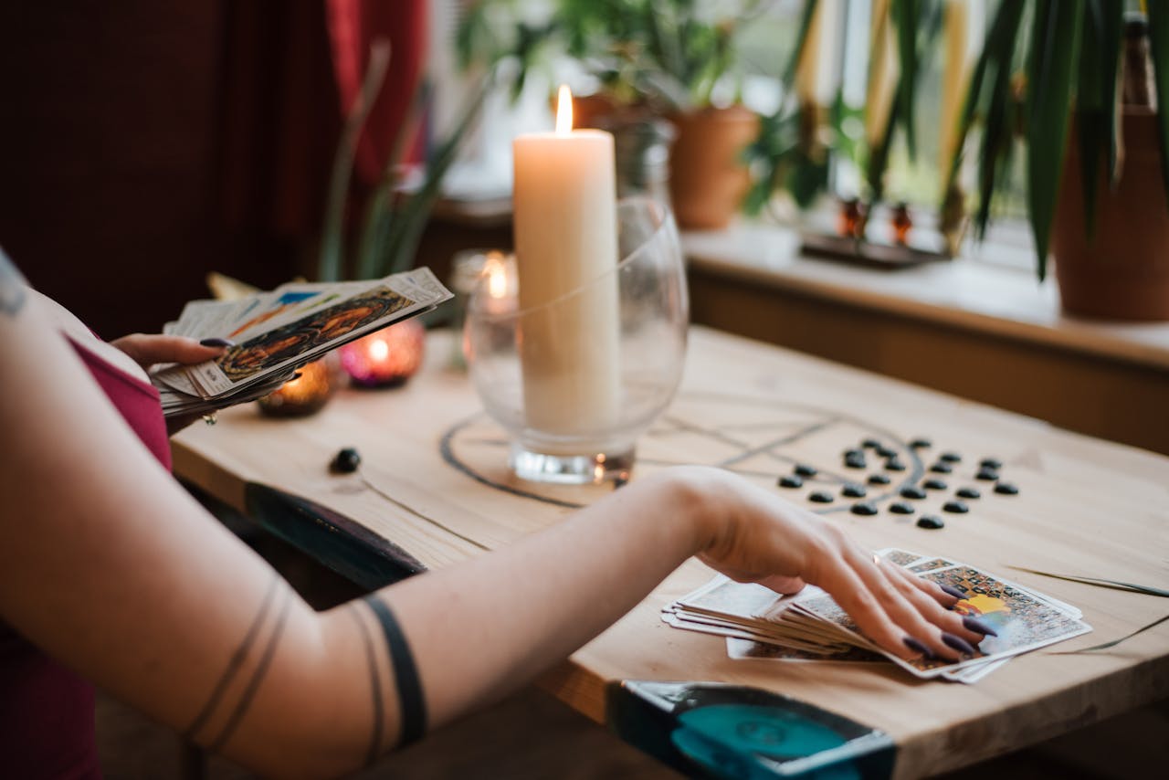 Crop unrecognizable fortune teller predicting fate with tarot cards near shiny candle at home